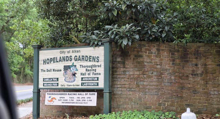 Hopelands Gardens entrance sign with serpentine brick wall and oak canopy in Aiken, SC