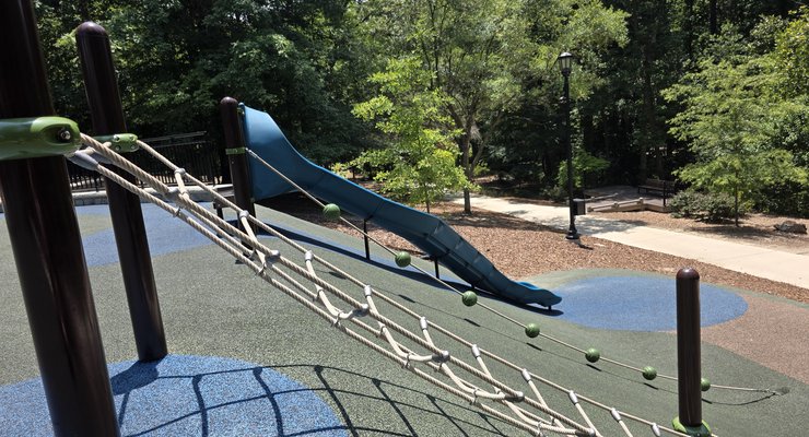 Rope bridge climbing feature and blue slide with paved trail visible at Virginia Hylton Park in Lexington SC