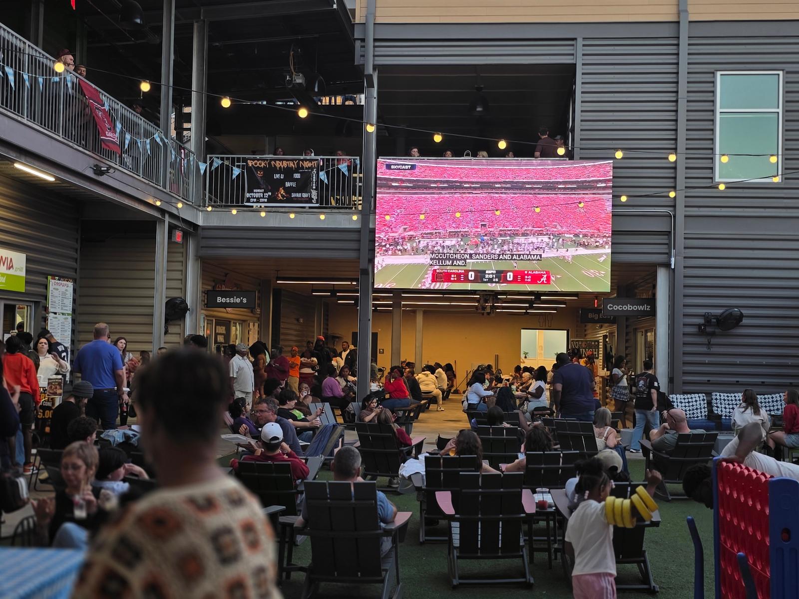Families relax on the patio watching the South Carolina Gamecocks game on the big screen inside Gather COLA