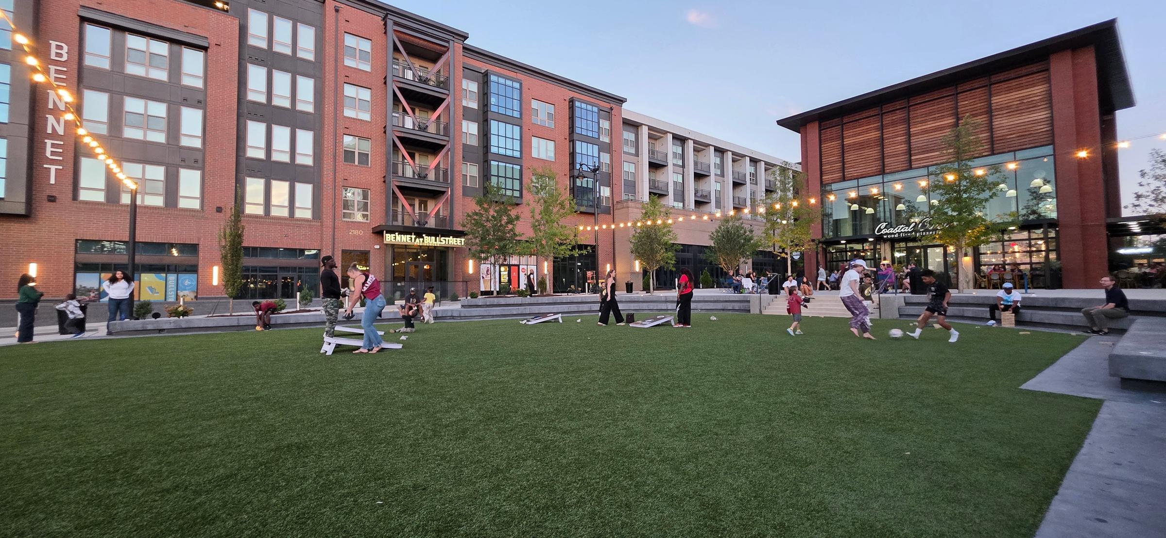 Kids play soccer and cornhole on the turf lawn outside Gather COLA in Columbia's BullStreet District