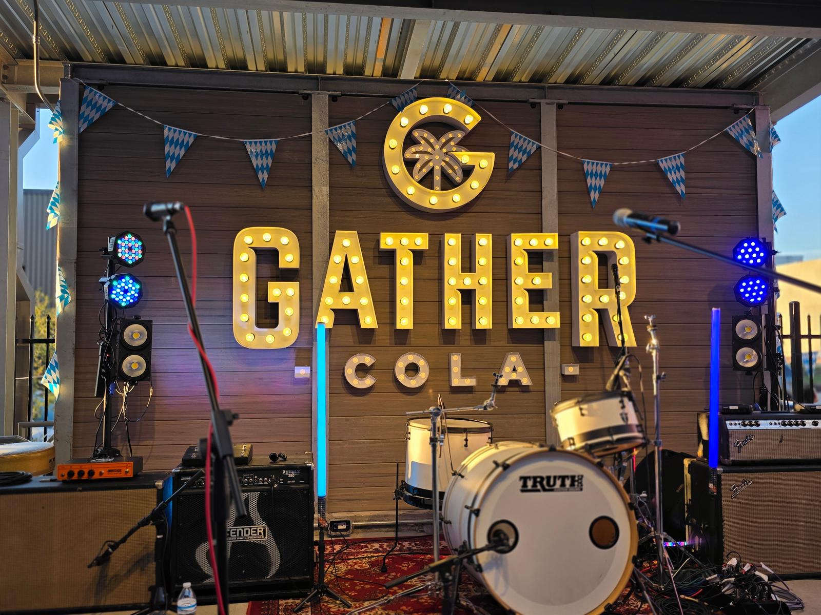 A live band's setup in front of the lit-up Gather COLA sign on the upstairs stage